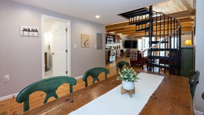 A dining area with a wooden table, green chairs, and a white rug. A staircase with wooden railings leads to an upper level. - Awesome Lakefront House on West Point Lake in LaGrange, Ga (Lagrange)