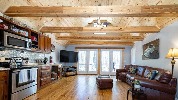 A spacious living area with wooden flooring, a brown leather sofa, a television, and a kitchen with wooden cabinets and a microwave. - Awesome Lakefront House on West Point Lake in LaGrange, Ga (Lagrange)