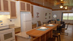Una cocina con armarios de madera, un refrigerador blanco, una estufa y un comedor con mesa y sillas.