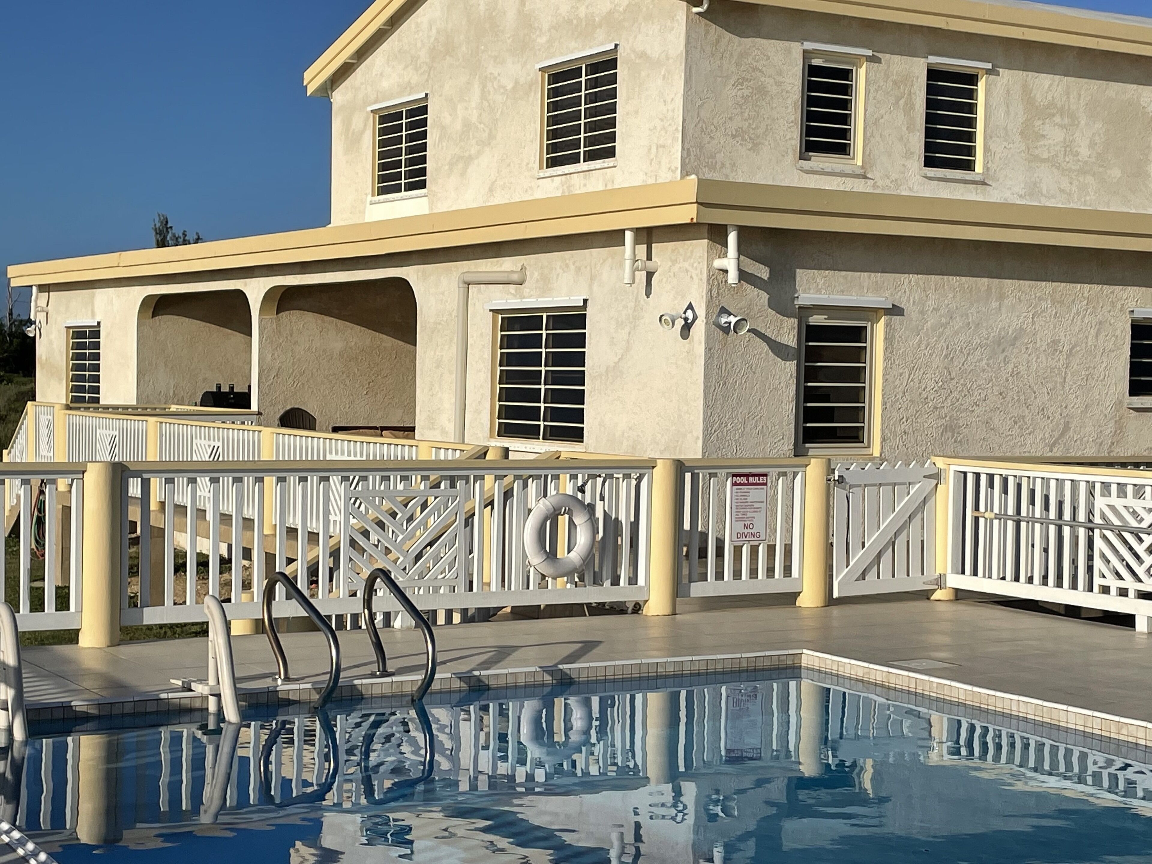 A pool area with a lifeguard stand, pool rules sign, and a building with multiple windows and a covered patio.