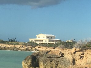 A large, two-story house with a flat roof, situated on a rocky cliff overlooking the ocean. - PARADISE COVE SECLUDED PRISTINE VILLA, "MARGARITA" (Frederiksted, St. Croix)