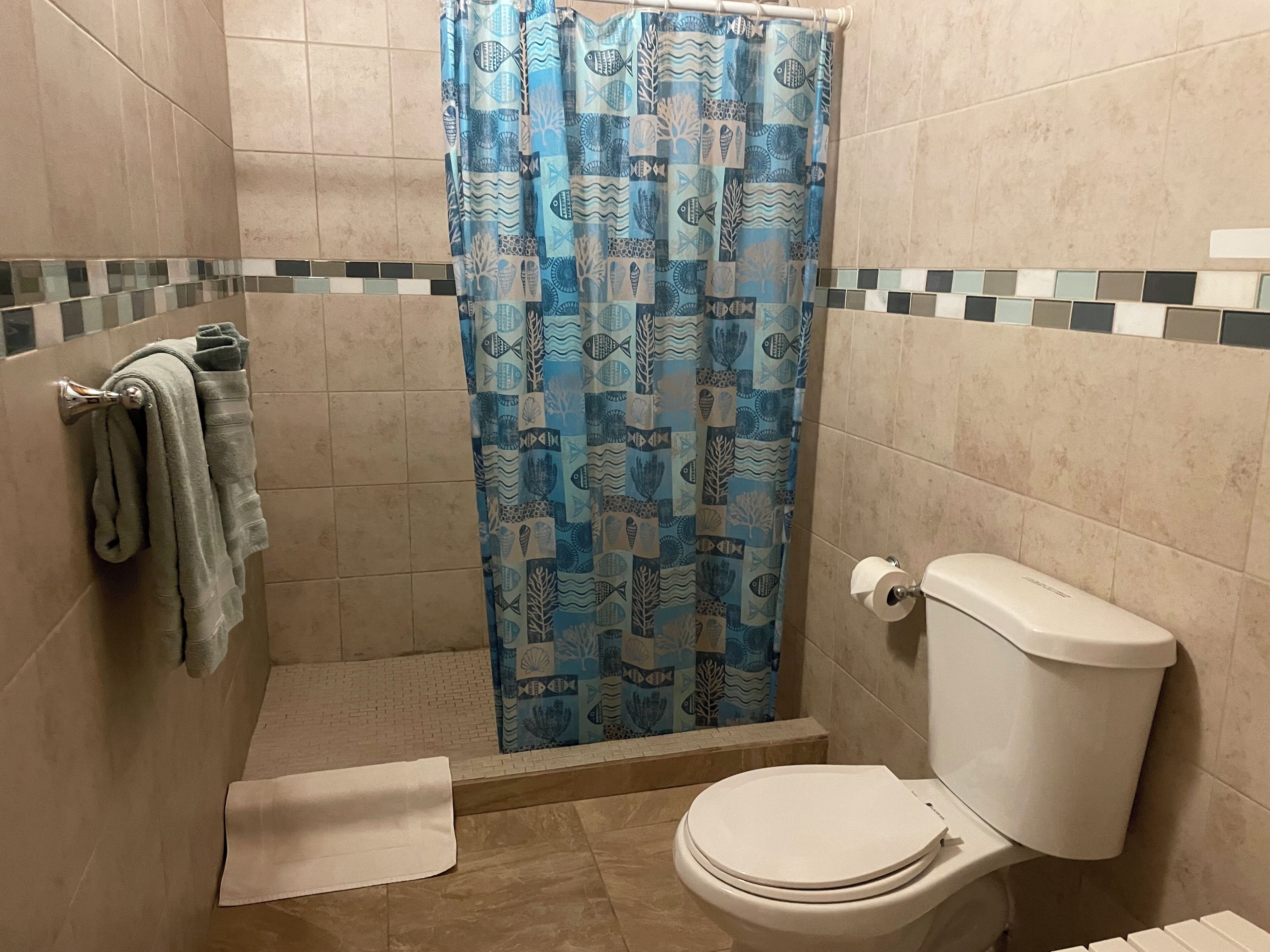 A bathroom with a shower curtain featuring a fish pattern, a toilet, and a towel rack with towels.