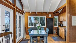 Uma área de refeições com uma mesa e cadeiras, um relógio na parede e vista para o exterior por grandes janelas.