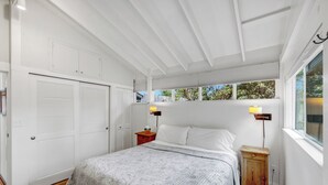 Quarto com cama, mesa de cabeceira, armário de madeira, janela com persianas e porta com venezianas.