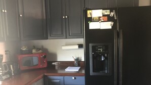 A compact kitchen with dark cabinets, a black refrigerator, a red microwave, and a coffee maker. - Family Friendly, Located Between Two Ski Hills, cable tv, WiFi, Off Road Parking (Laurium)