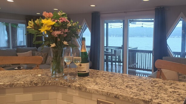 Comedor con encimera de granito, un florero con flores, una botella de champán y vista al agua a través de amplias ventanas.