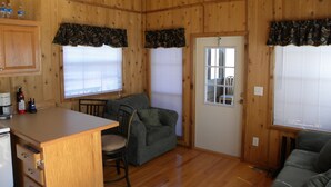 A wooden cabin interior with a kitchenette, a sofa, a dining table, and a door with a window.