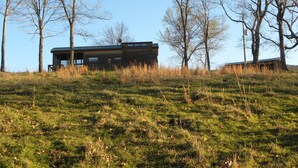 A modern building with a flat roof, surrounded by tall trees and grassy terrain.