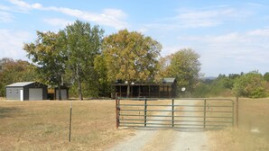 A rural property with a gravel driveway leading to a gated entrance, surrounded by trees and a small building.