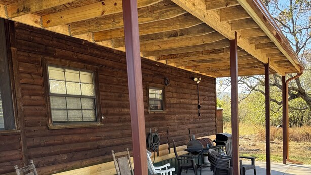 A log cabin with a covered porch, outdoor seating, and a grill area.