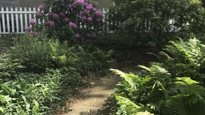 A garden path leading to a house with a satellite dish, a window, and a white picket fence. - Beautiful Private Harbert Beach cottage well appointed on a quiet private lane (Harbert)