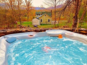 Un jacuzzi con un patito de goma, rodeado de un muro de piedra, con una casa y árboles al fondo.