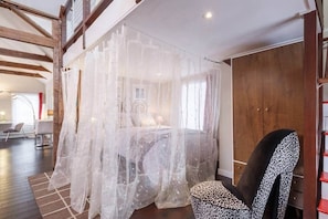 Un dormitorio con cama con dosel, un sillón estampado de leopardo y un armario de madera.
