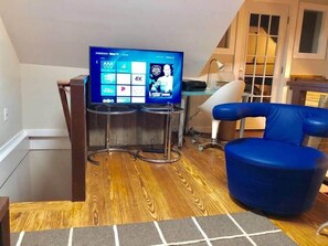 Una sala de estar moderna con un televisor de pantalla plana, un sillón azul y piso de madera.