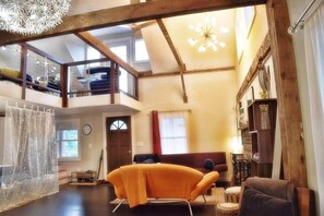 A spacious loft-style room with a high ceiling, a mezzanine level, and a large window.