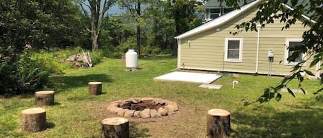 A house with a fire pit in the yard, surrounded by trees and a clear sky.