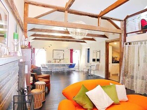 Una habitación con techo de madera, un sofá con cojines, un tambor y una zona de comedor al fondo.