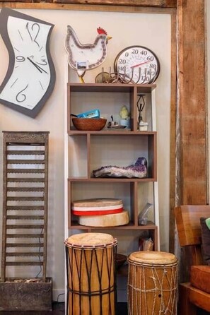 Un interior rústico con un reloj de pared, un gallo decorativo, estantes con diversos objetos y dos tambores.