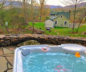 Un jacuzzi con una pared de piedra y una casa al fondo.