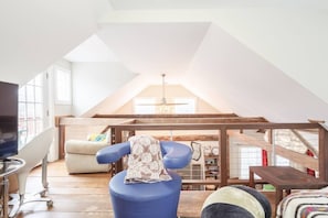 An attic room with a sloped ceiling, a television, a blue chair, and a sofa.