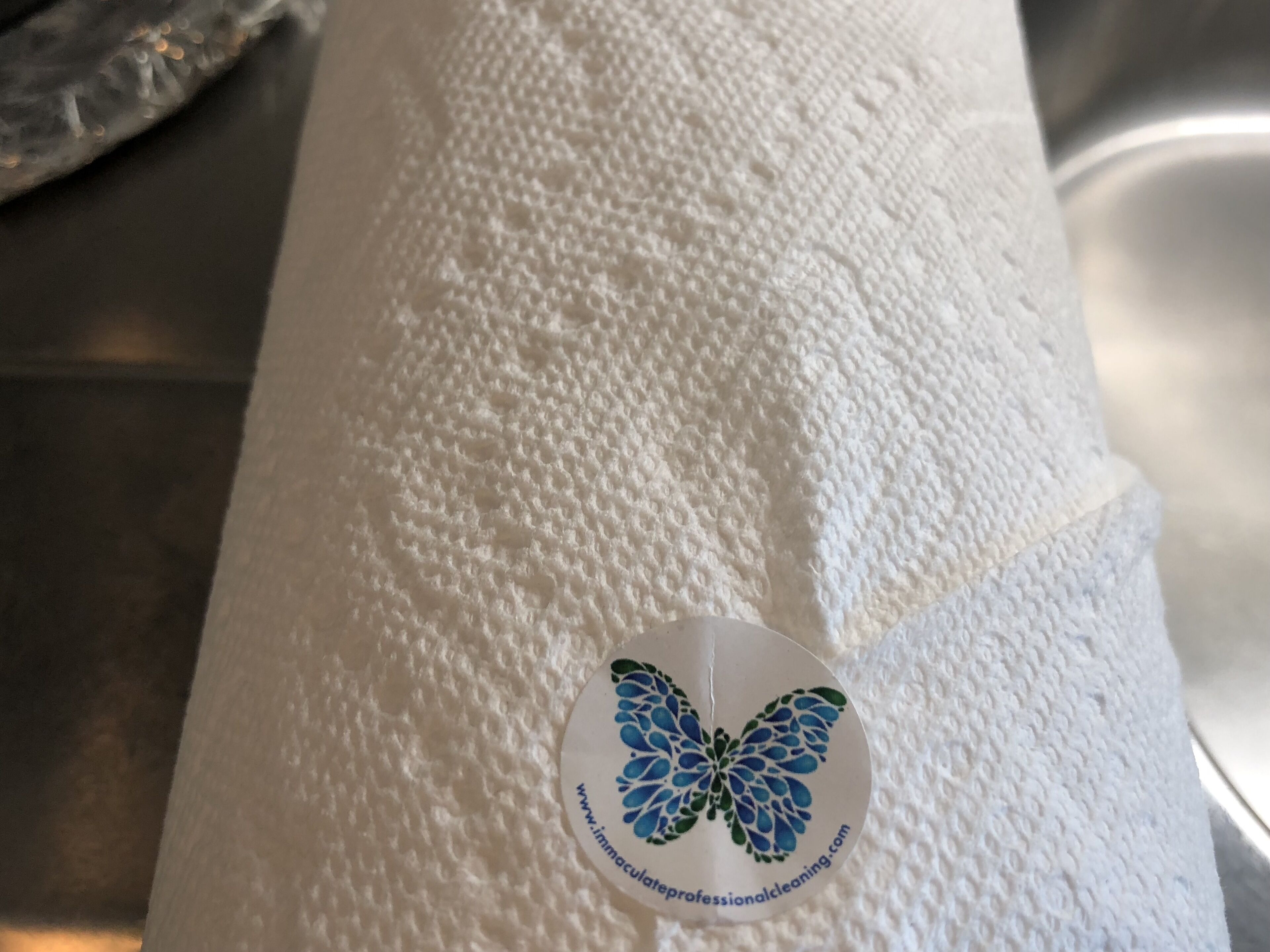 Superficie blanca texturizada con un adhesivo circular que muestra un diseño de mariposa azul y texto.