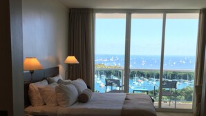 A hotel room with a large bed, two bedside lamps, a chair, and a view of a marina with boats.
