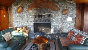 A cozy living room with stone walls, a fireplace, two green leather sofas, and a coffee table. - Heart Stopping Ocean Views, Secluded Getaway, Whale Watching (Little River)