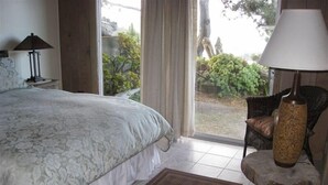 A bedroom with a bed, a nightstand, a lamp, a chair, and a view of the outdoors. - Heart Stopping Ocean Views, Secluded Getaway, Whale Watching (Little River)