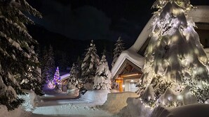 A snow-covered landscape with a building featuring a sloped roof and a lit Christmas tree. - Whistler Mountainside Ski-In Ski-Out Spectacular Views (Whistler)