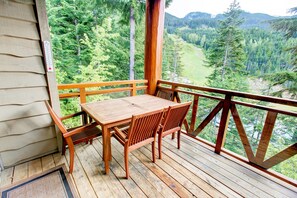 A wooden deck with a table and chairs, overlooking a forested valley. - Whistler Mountainside Ski-In Ski-Out Spectacular Views (Whistler)