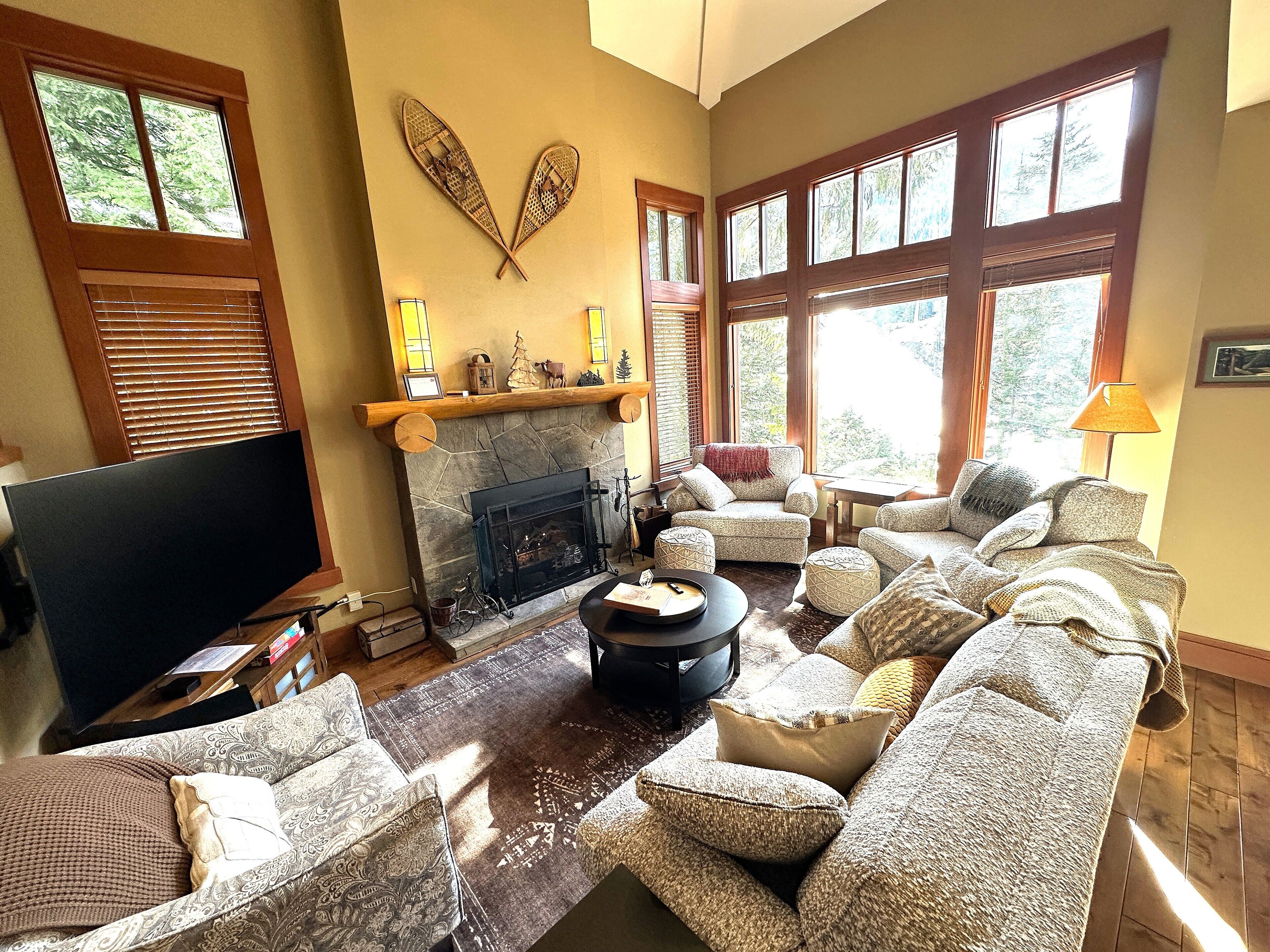A cozy living room with a fireplace, comfortable seating, and large windows.