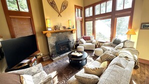 A cozy living room with a fireplace, comfortable seating, and large windows. - Whistler Mountainside Ski-In Ski-Out Spectacular Views (Whistler)