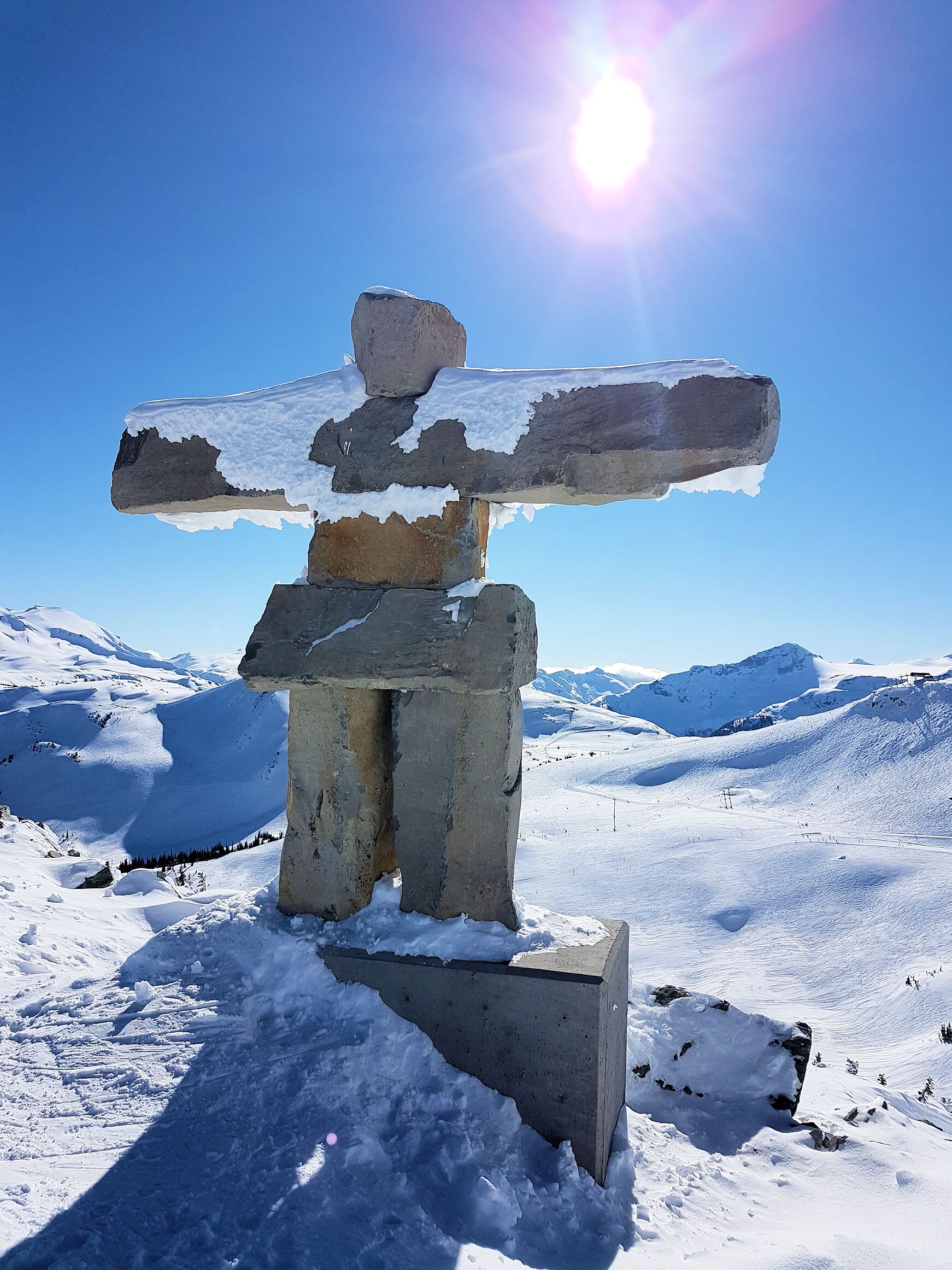 A totem pole in a snowy landscape with mountains in the background.