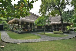 A thatched-roof house with a stone pathway, surrounded by lush greenery and a well-maintained lawn. - Exotic Beachfront Villa in the Serene North (Pemuteran)