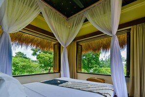 A bedroom with a bed, white curtains, and a view of greenery outside. - Exotic Beachfront Villa in the Serene North (Pemuteran)