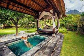 Un área de piscina con una pérgola, una tumbona y una persona relajándose en el agua.