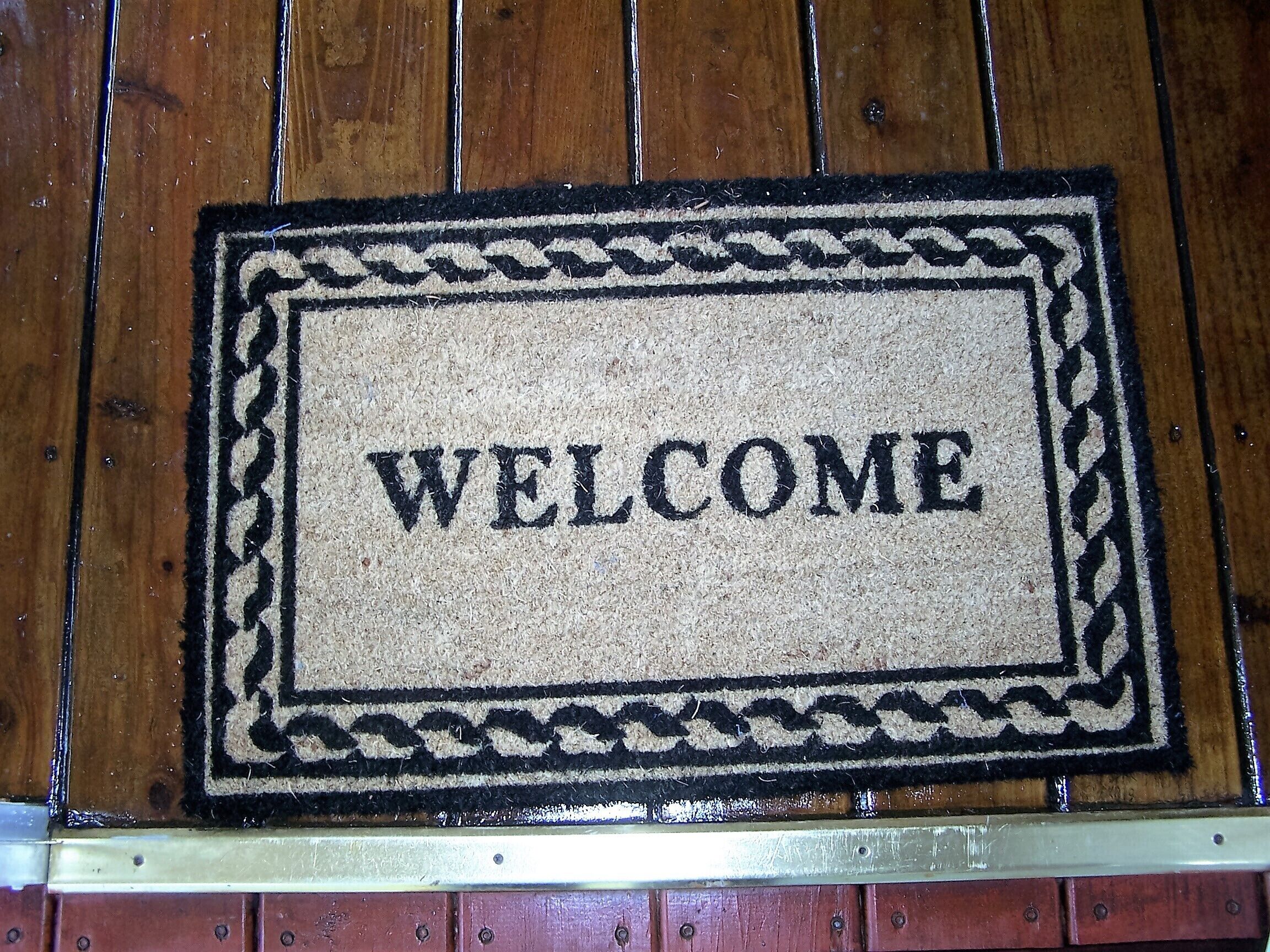 A welcome mat with the word "WELCOME" in the center, placed on a wooden floor.