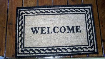 A welcome mat with the word "WELCOME" in the center, placed on a wooden floor.