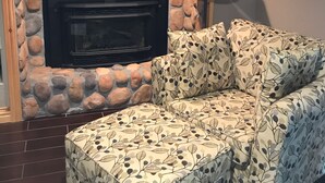 A living room with a stone fireplace, a sofa with a leaf pattern, and a wooden shelf above the fireplace. - Most Beautiful View on Table Rock Lake! (Shell Knob)