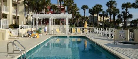 A swimming pool with a 5 FT depth marker, surrounded by palm trees and a covered seating area with white railings.