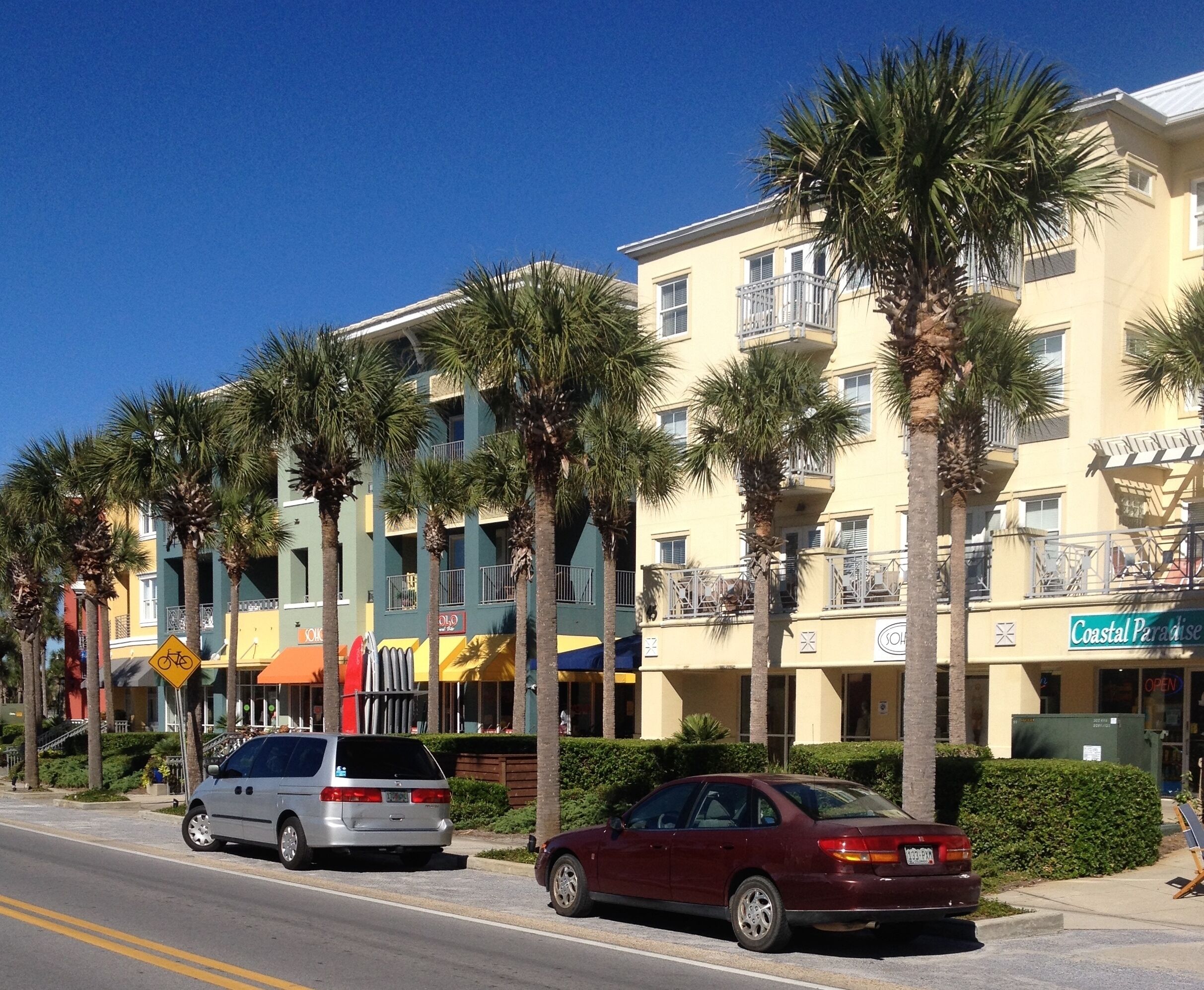 A multi-story hotel with balconies, palm trees, and a sign for 'Coastal Paradise'.