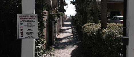 A pathway leading to a building labeled "GULF PLACE" with a sign indicating no lifeguard on duty and a flag system for hazard levels.