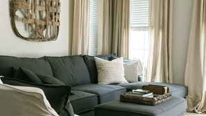 A living room with a sectional sofa, a white armchair, a coffee table, and a decorative wall piece. - The Guesthouse at The Waters, Walk to Chapel, Pool & Town Square (Pike Rd)