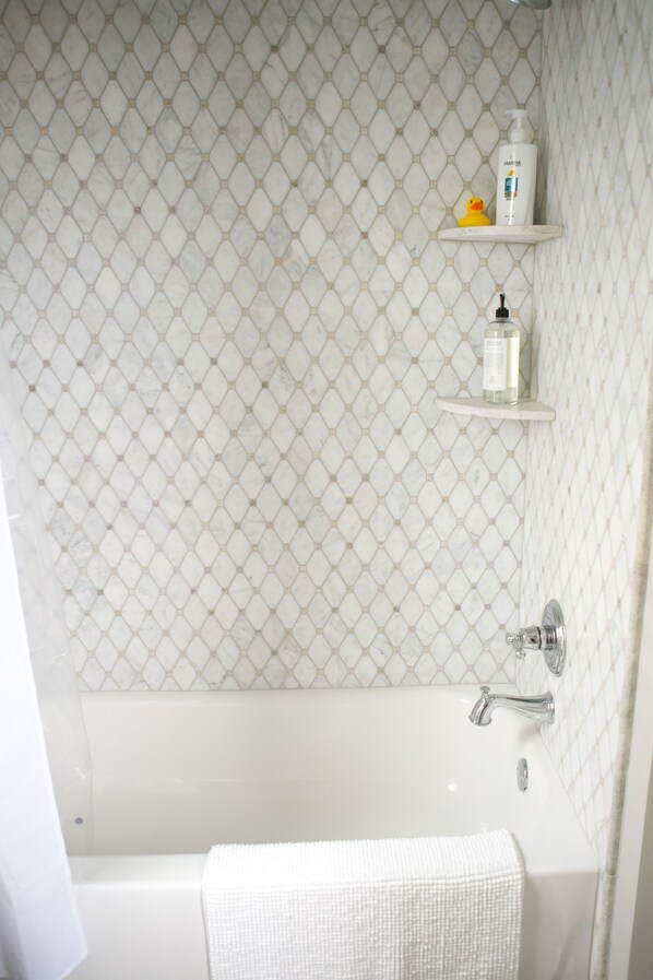 A bathroom with a white bathtub, a white towel, and a shelf with toiletries. - The Guesthouse at The Waters, Walk to Chapel, Pool & Town Square (Pike Rd)