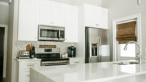 A modern kitchen with white cabinetry, stainless steel appliances, and a large island with a sink. - The Guesthouse at The Waters, Walk to Chapel, Pool & Town Square (Pike Rd)