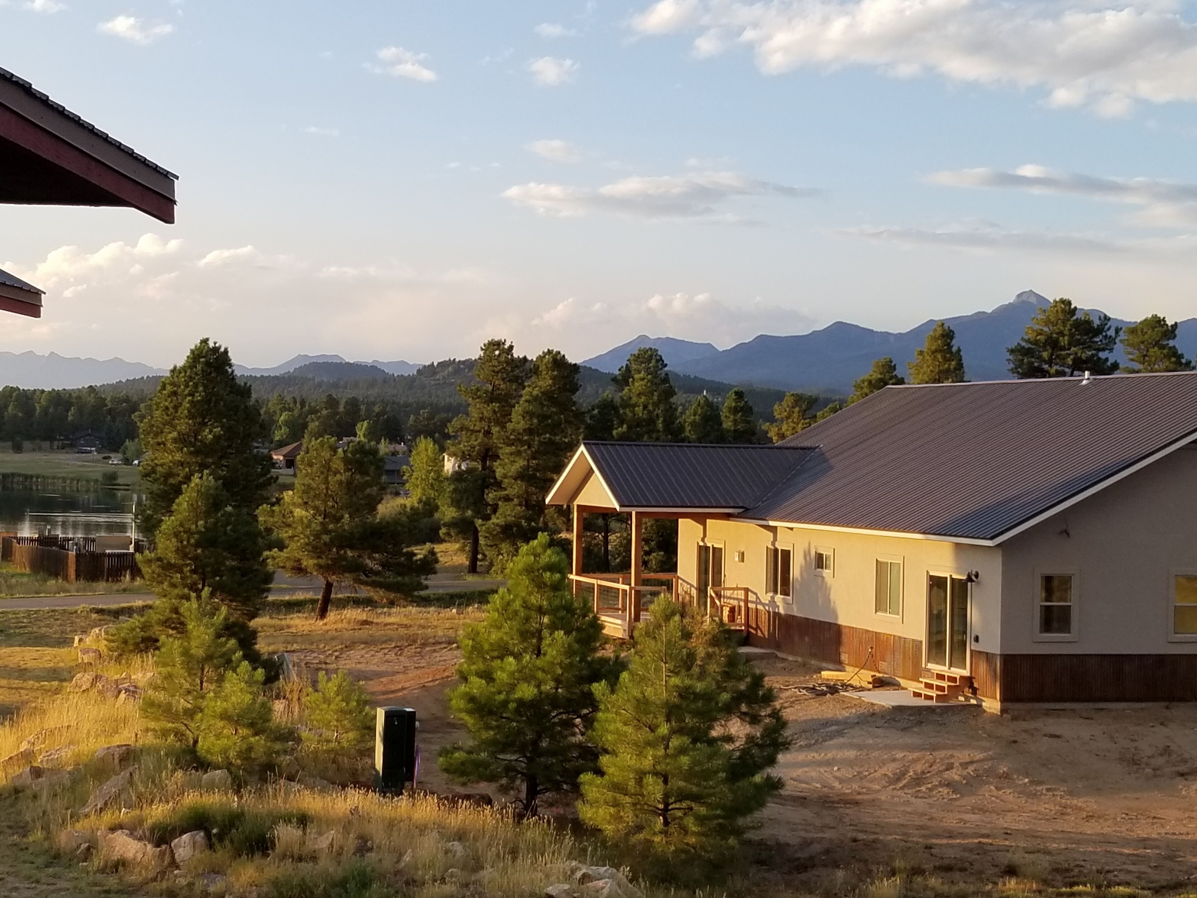 A house with a covered porch, surrounded by trees and a mountainous backdrop.