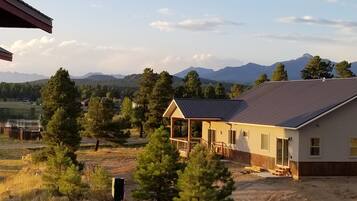 A house with a covered porch, surrounded by trees and a mountainous backdrop.