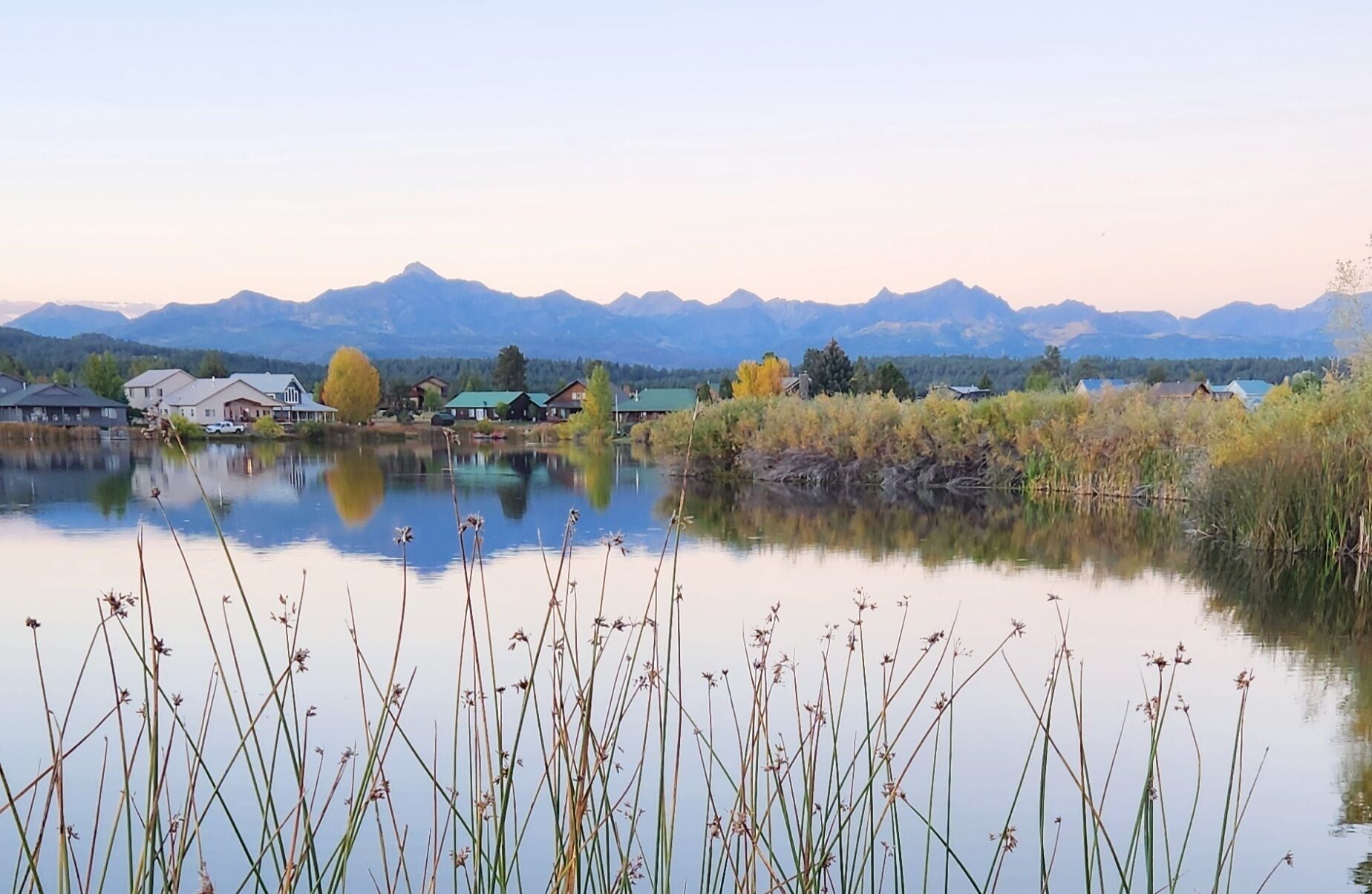 A tranquil lakeside view with houses and mountains in the background.
