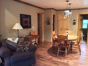 A living room with a sofa, a dining table with chairs, a lamp, and a framed picture on the wall. - LIL' LAZY BEAR LODGE (Danbury)