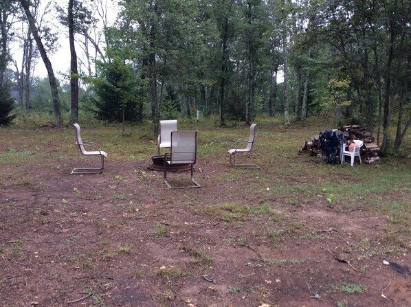 An outdoor seating area with metal chairs and a bench, surrounded by trees. - LIL' LAZY BEAR LODGE (Danbury)